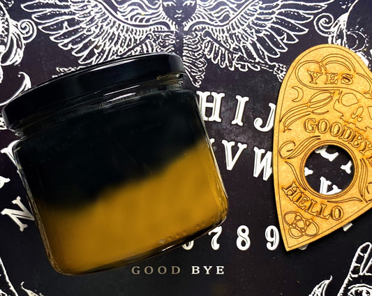 Back view of the Ouija candle's black-to-amber ombre wax jar on a Ouija board