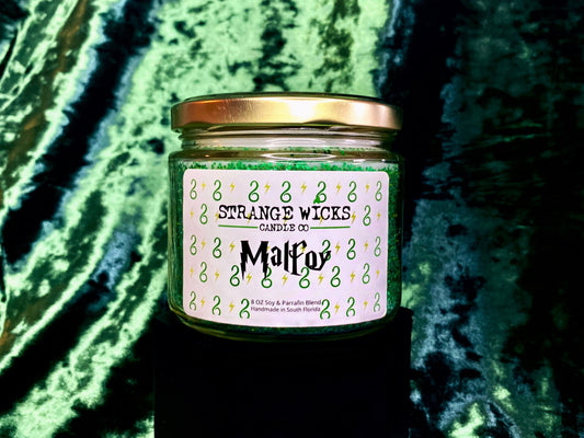 Malfoy Candle label close-up with gold lid on green satin backdrop