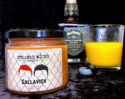 Gallavich candle with lid beside a whiskey bottle and glass of orange juice